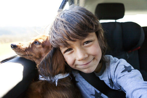 Portrait of smiling little boy sitting with his long-haired dachshund in a car stock photo