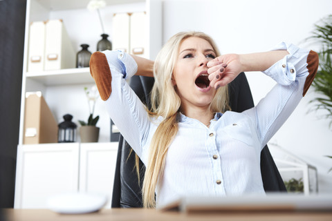 Porträt einer blonden Frau, die an ihrem Schreibtisch gähnt, lizenzfreies Stockfoto