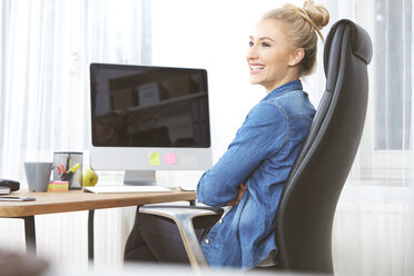 Lächelnde blonde Frau sitzt am Schreibtisch in ihrem Büro zu Hause - SEGF000511