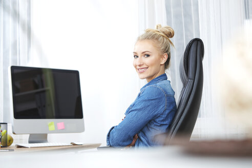 Porträt einer lächelnden blonden Frau, die am Schreibtisch in ihrem Büro sitzt - SEGF000512