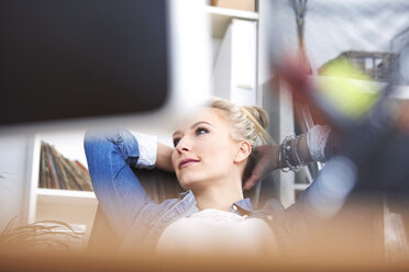 Lächelnde blonde Frau entspannt sich mit den Händen hinter dem Kopf am Schreibtisch im Büro - SEGF000513