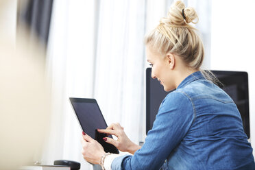 Blonde Frau sitzt am Schreibtisch und benutzt ein digitales Tablet - SEGF000514