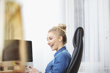 Lachende blonde Frau, die am Schreibtisch sitzt und ein digitales Tablet benutzt - SEGF000515
