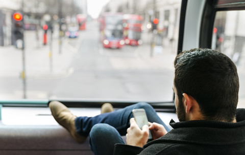 Großbritannien, London, junger Mann in einem Doppeldeckerbus, der sein Smartphone benutzt, lizenzfreies Stockfoto