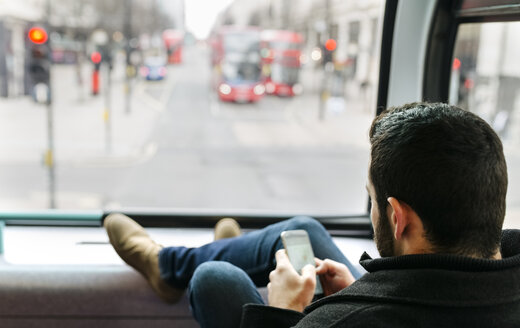 UK, London, young man in a double-decker bus using his smartphone - MGOF001694