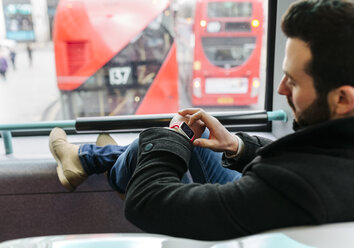 UK, London, young man in a double-decker bus using his smartwatch - MGOF001695