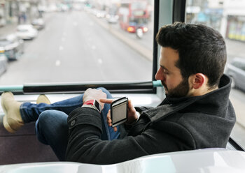 UK, London, young man in a double-decker bus using his smartwatch - MGOF001696