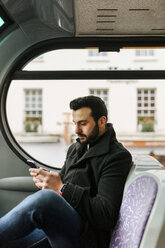 Junger Mann in einem Doppeldeckerbus, der sein Smartphone benutzt - MGOF001697