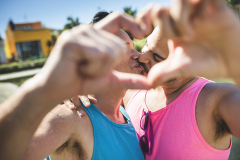 Kissing gay couple shaping heart with their fingers stock photo