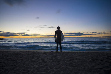 Rückansicht eines Surfers, der bei Sonnenaufgang am Strand steht - SKCF000080