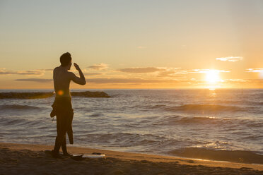 Rückenansicht eines Surfers, der am Strand steht und den Sonnenaufgang beobachtet - SKCF000084
