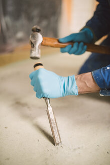 Bricklayer removing irregularities on floor screed with hammer and chisel - RAEF000993