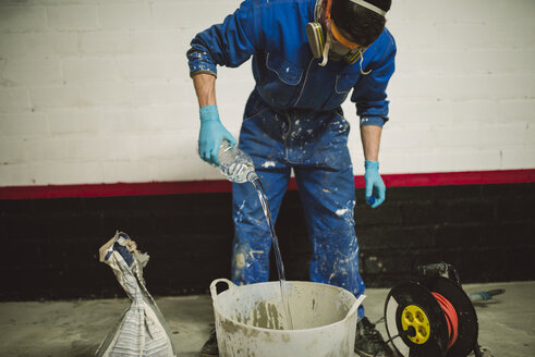 Bricklayer preparing cement in bucket, pouring water from bottle - RAEF001005