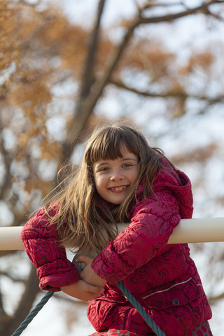 Porträt eines lächelnden kleinen Mädchens, das auf ein Spielplatzgerät klettert, lizenzfreies Stockfoto