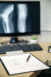 Nahaufnahme eines medizinischen Berichts auf einem Tisch und eines Röntgenbildes auf einem Computerbildschirm - DAPF000058