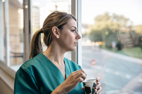 Frau im Kittel macht Kaffeepause und schaut aus dem Fenster, lizenzfreies Stockfoto