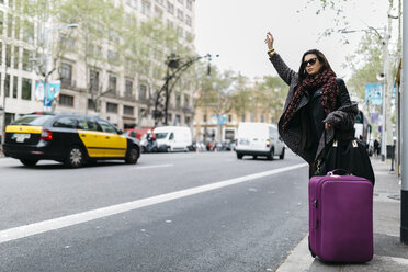 Spanien, Barcelona, junge Frau mit Koffer, die ein Taxi ruft - JRFF000510