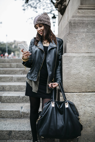 Lächelnde junge Frau, die im Freien auf ihr Handy schaut, lizenzfreies Stockfoto