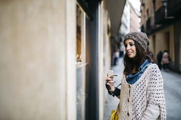 Spain, Barcelona, smiling young woman in the city looking at shop window - JRFF000523