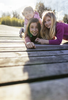 Gruppenbild von drei Mädchen auf einer Strandpromenade, die lustige Gesichter ziehen - MGOF001709