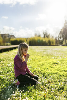 Kleines Mädchen hockt auf einer Wiese und riecht an Gänseblümchen - MGOF001712