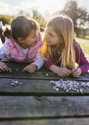 Two little girls lying on a boardwalk looking at each other - MGOF001717