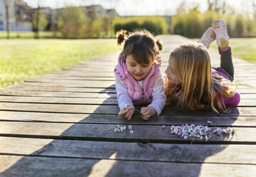 Zwei kleine Mädchen liegen auf einer Promenade und schauen sich an - MGOF001718