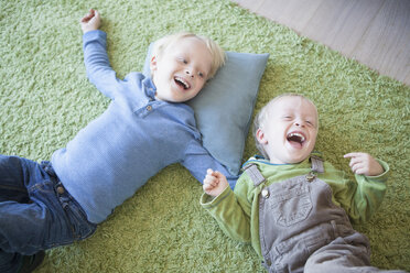 two laughing little brothers lying on green carpet at home - RBF004245