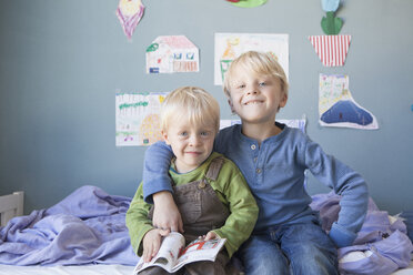 Porträt von zwei kleinen Brüdern, die auf dem Bett eines Kinderzimmers sitzen - RBF004247