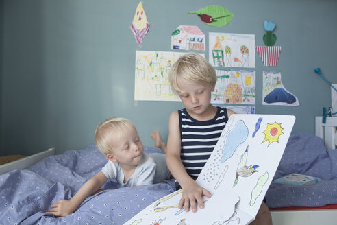Zwei kleine Brüder auf dem Bett im Kinderzimmer beim Betrachten eines Bilderbuchs - RBF004252