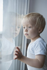 Porträt eines kleinen blonden Jungen, der durch ein Fenster schaut - RBF004254