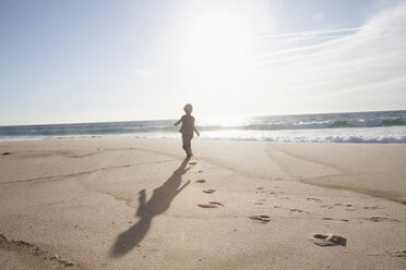 Rückenansicht eines Jungen, der in der Dämmerung am Strand läuft - RBF004259