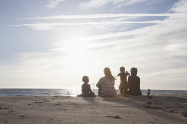 Rückenansicht einer Familie mit zwei Kindern, die in der Dämmerung am Strand sitzen - RBF004262