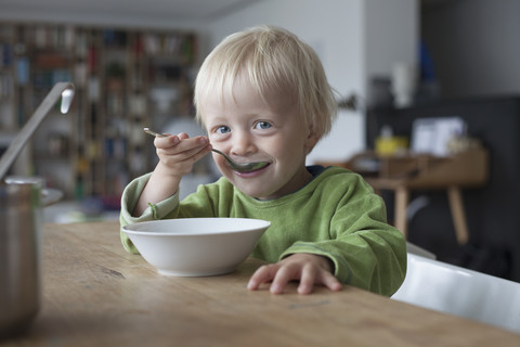 Porträt eines lächelnden kleinen Jungen, der zu Hause eine Suppe isst, lizenzfreies Stockfoto