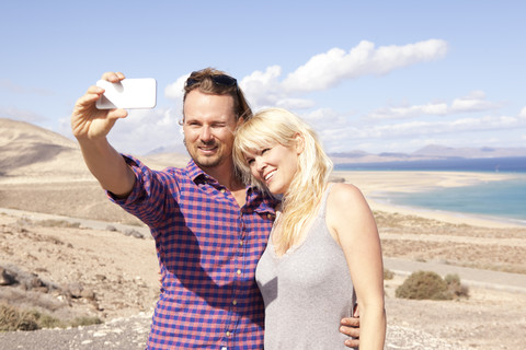 Spanien, Fuerteventura, Jandia, Paar macht Selfie an der Küste, lizenzfreies Stockfoto