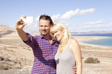 Spain, Fuerteventura, Jandia, couple taking selfie at the coast - MFRF000592