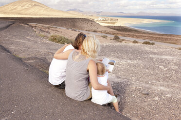 Spanien, Fuerteventura, Jandia, Familie sitzt an der Küste und schaut in den Reiseführer - MFRF000597