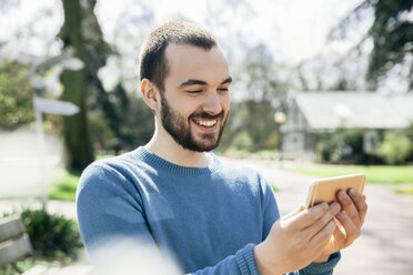 Porträt eines lächelnden jungen Mannes, der auf sein Smartphone schaut - MFF002965