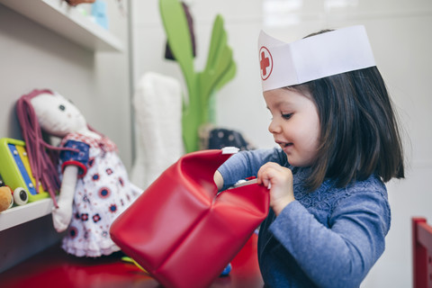 Kleines Mädchen sucht medizinisches Spielzeug in einer roten Tasche, lizenzfreies Stockfoto