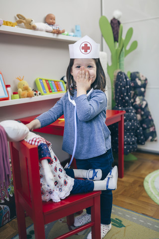 Porträt eines kleinen Mädchens, das mit medizinischem Spielzeug spielt und sein Gesicht mit der Hand bedeckt, lizenzfreies Stockfoto