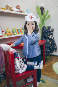 Porträt eines kleinen Mädchens, das mit medizinischem Spielzeug spielt und sein Gesicht mit der Hand bedeckt - DAPF000081