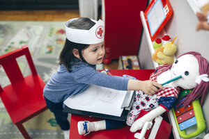 Kleines Mädchen mit Krankenschwesternmütze zeichnet ihre Puppe - DAPF000084