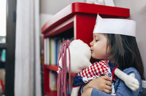 Kleines Mädchen, das seine Puppe umarmt und küsst, lizenzfreies Stockfoto