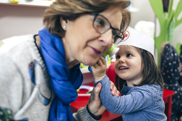 Portrait of little girl examining ear of her grandmother with medical toys - DAPF000088