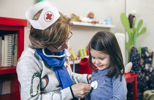 Ältere Frau mit Krankenschwestermütze untersucht ihre Enkelin mit einem Spielzeugstethoskop - DAPF000090