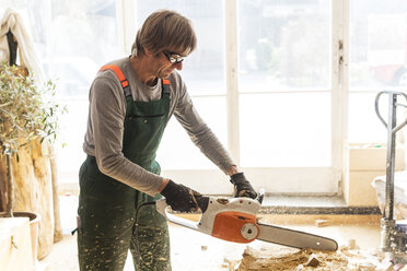 Wood carver in workshopworking on wood for a sculpture with a chainsaw - TCF004943