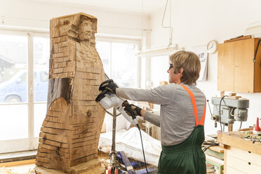 Holzschnitzer in der Werkstatt bei der Arbeit an einer Skulptur mit der Kettensäge - TCF004952