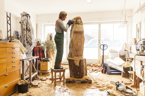 Holzschnitzer in der Werkstatt bei der Arbeit an einer Skulptur mit einer Fräsmaschine, auf einem Hocker stehend - TCF004958