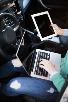 Woman working inside her car with digital tablet and laptop - JPF000120