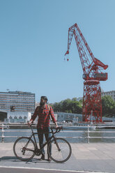 Spain, Bilbao, man and his racing cycle in front of harbour crane - RTBF000097